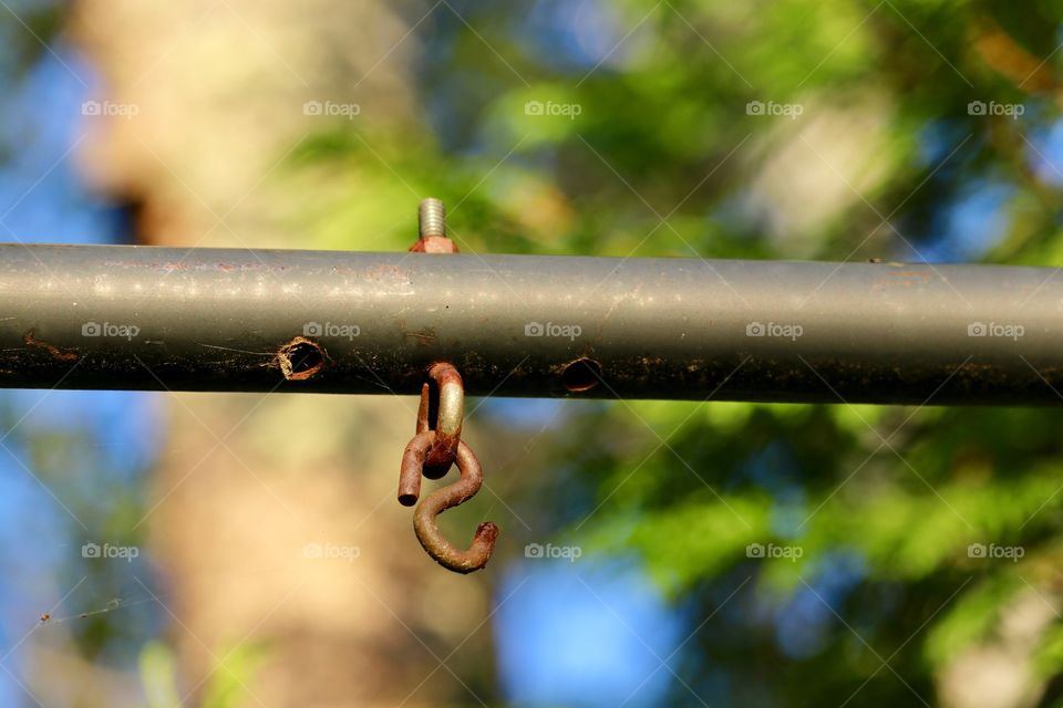 Rusted S-ring hanging off metal pole outdoors 