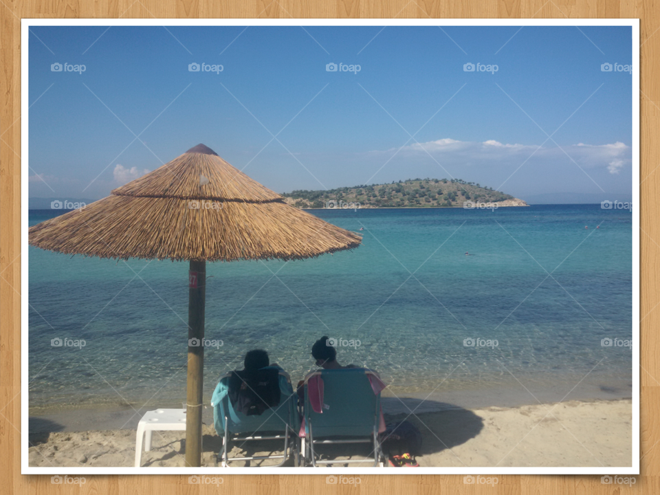 sandy beach and blue sea with sunbed and people sitting in it