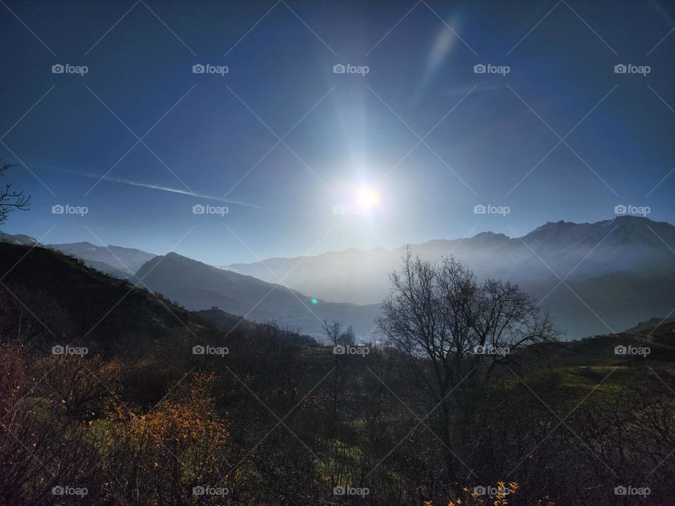 A majestic allure of the mountains, bathed in the gentle embrace of the morning sun. The radiant sunlight crowns the rugged peaks with a divine glow, as a veil of mist softens the valleys below, creating an ethereal, dreamlike atmosphere.