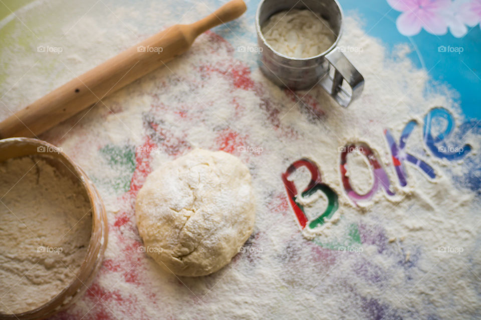 On the table lies a pastry for pies with sprinkled flour and a seeder for flour. Written to bake on the table.