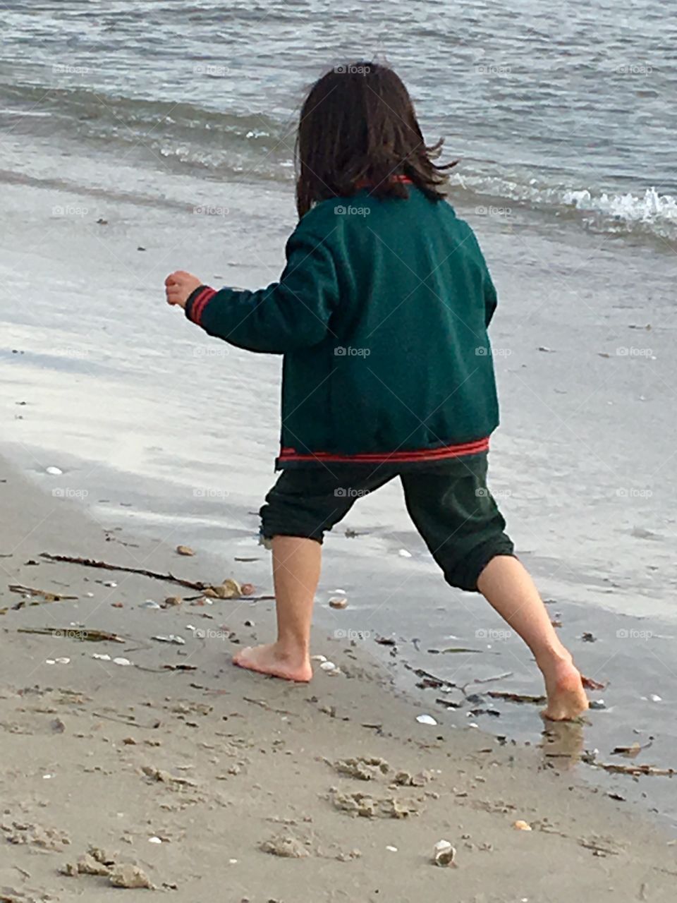 Barefoot little girl with dark hair playing on the beach on an overcast day 