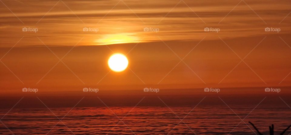 View on the sun that is seen between two layers of clouds looking like sunset over the sea