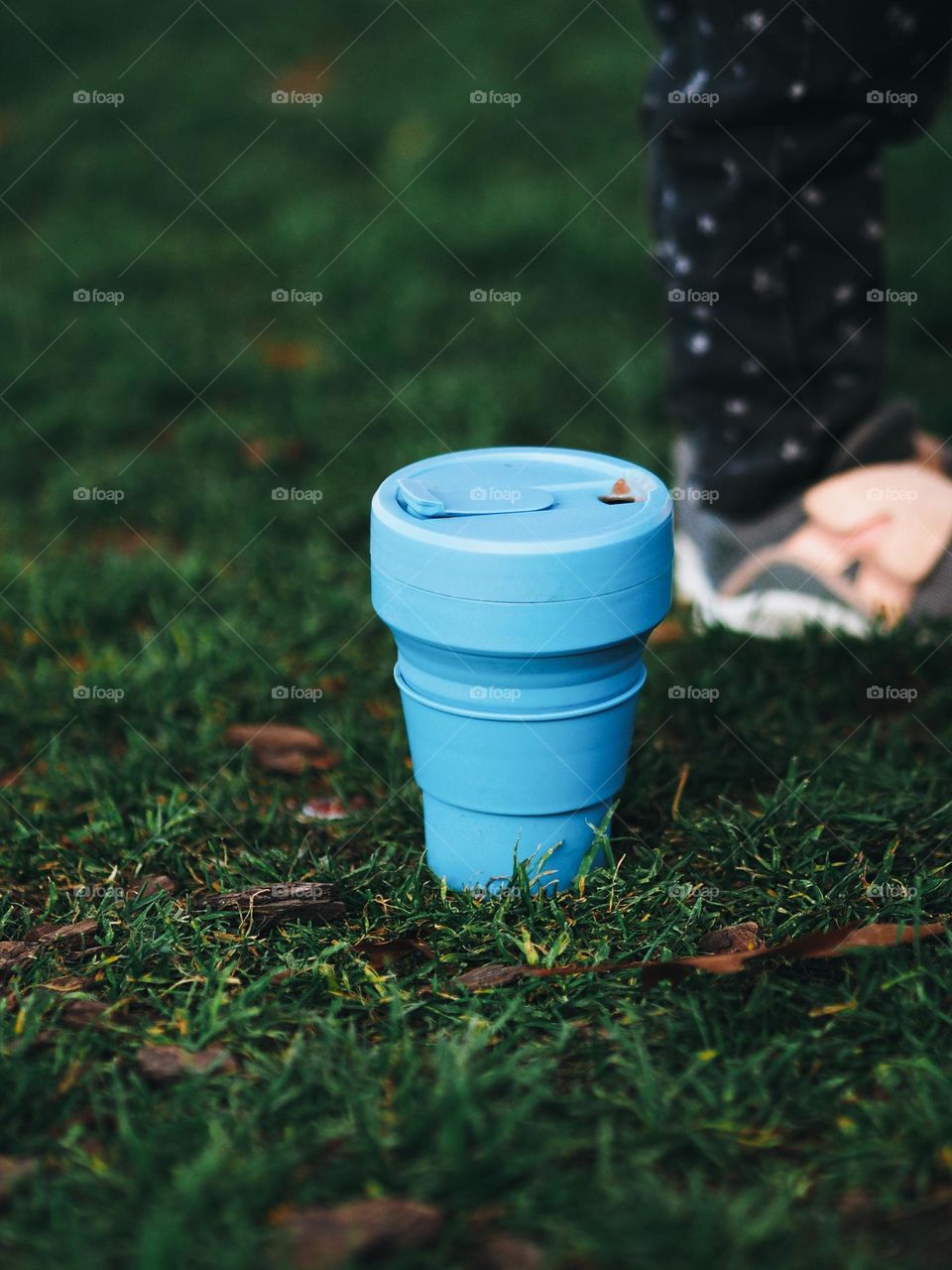 Blue reusable silicone cup for coffee or water stands on green grass, nobody 