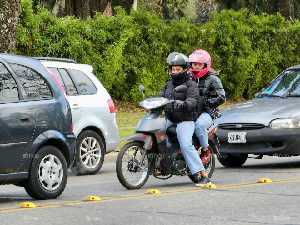 A couple on a motorbike waiting for traffic to move.  It's their choice of transportation; cheaper, personal, faster