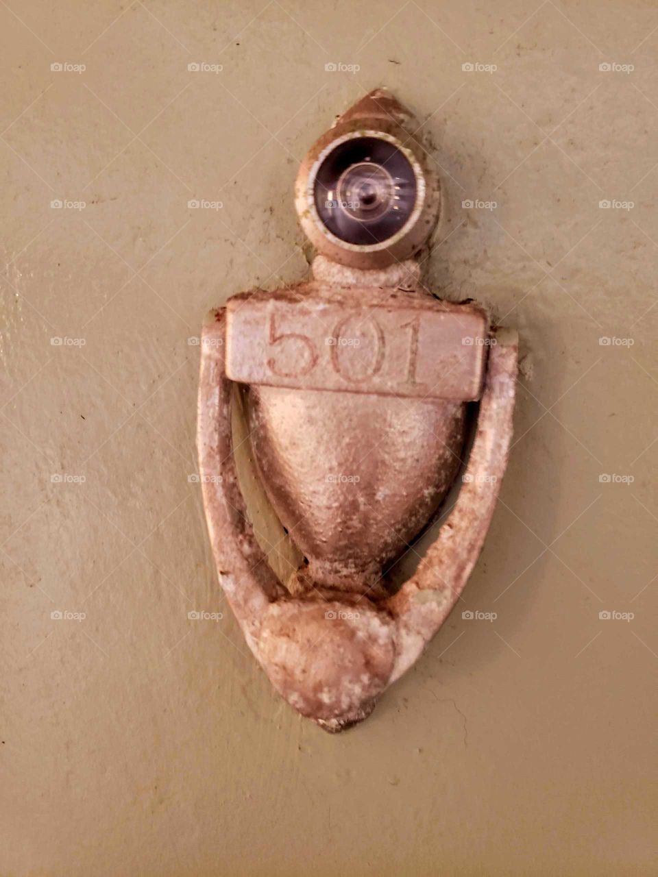 Brass door knocker, aged and roughened. Displaying the number 501 on an old metal door.
