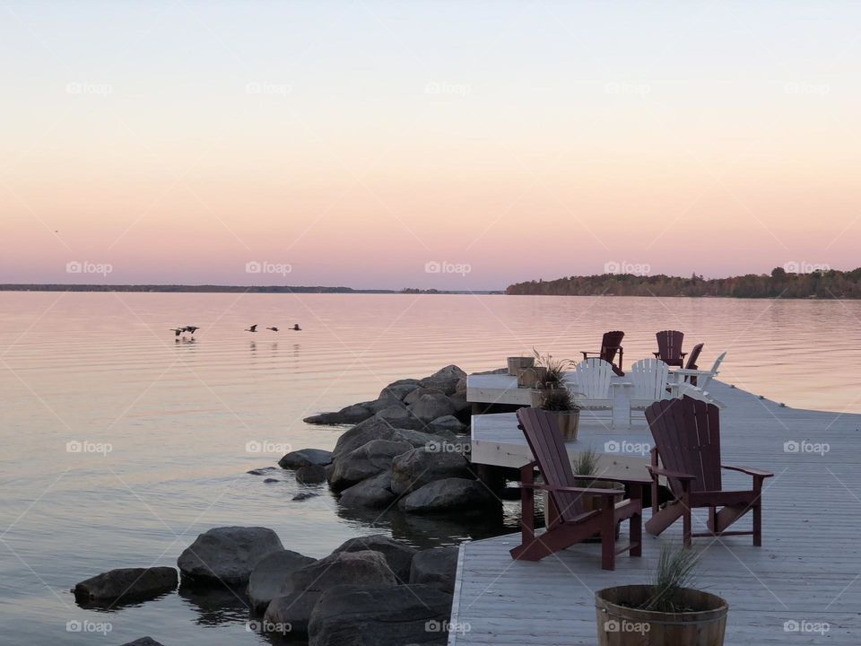 Cottage country Ontario , sunset in the fall , pier with muskoka chairs water and birds , peaceful and inviting 