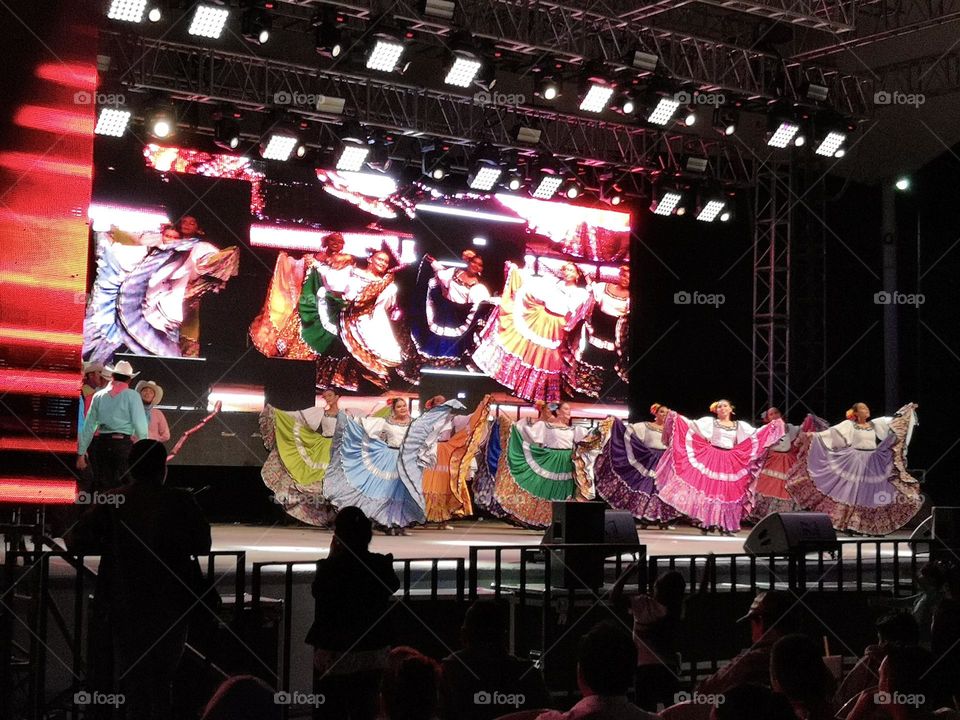 Women dressed with colorful skirts, dancing on a scenario.