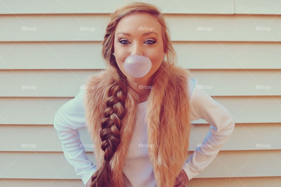 Young woman blowing chewing gum against wall