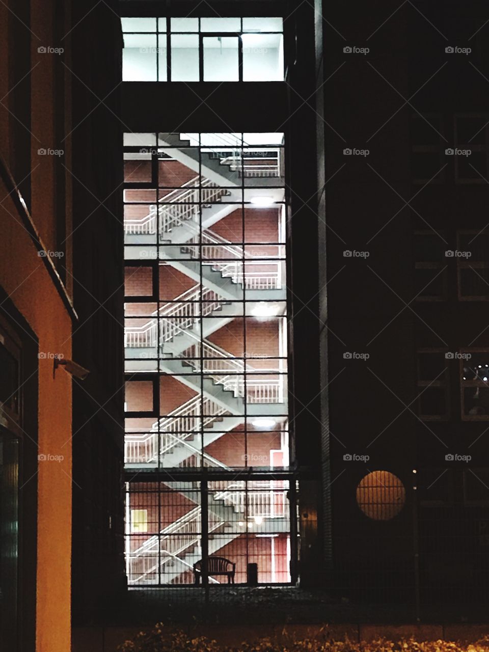 Zick-Zack Treppenhaus. Hell beleuchtete Treppen verlaufen symmetrisch hinter einer Glasfront.