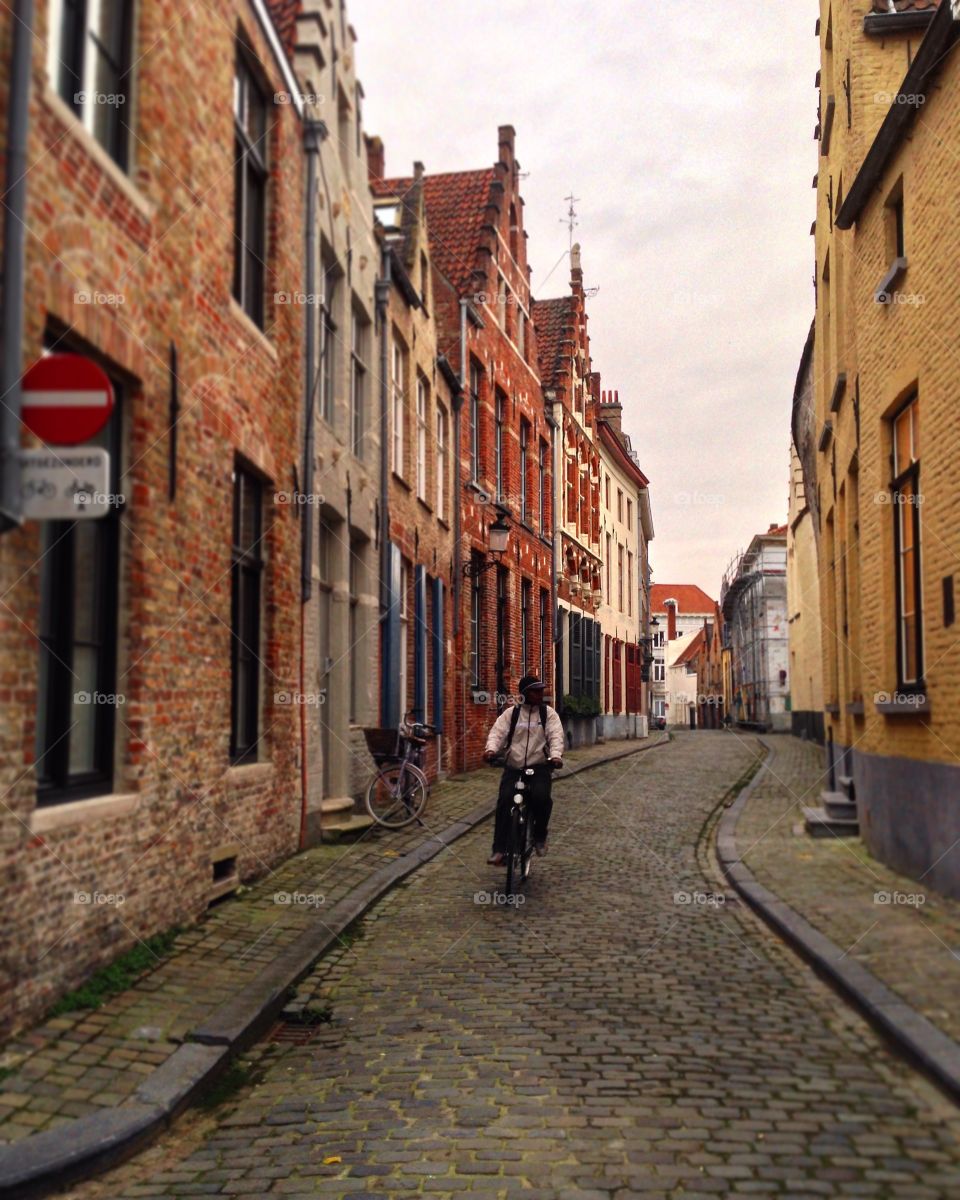 A man peacefully rides a bike through a cobblestone street of Brugge, Belgium. 
