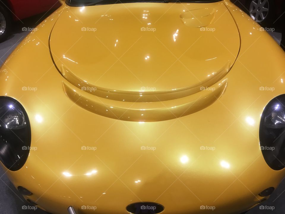 Front of a golden yellow TVR Tamora Convertable admired at the London Classic Car Show, Excel, in Winter. Appearance like an elliptic or robotic cartoon face.