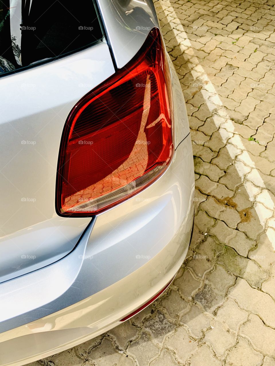 Red back light of a silver Volkswagen sedan taken while the ignition is off and car is parked.