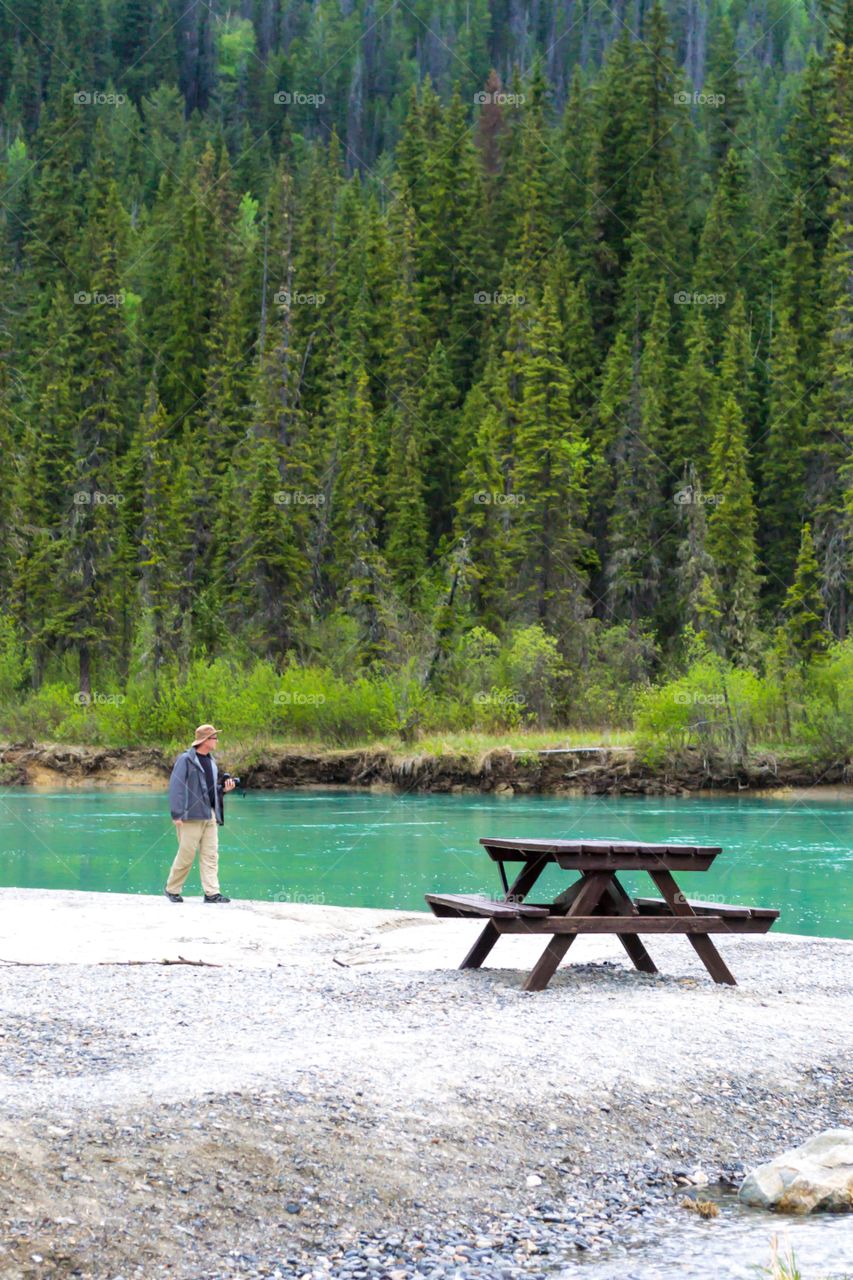 Male photographer with camera walking along Glacial fed river in Banff Alberta Canada 