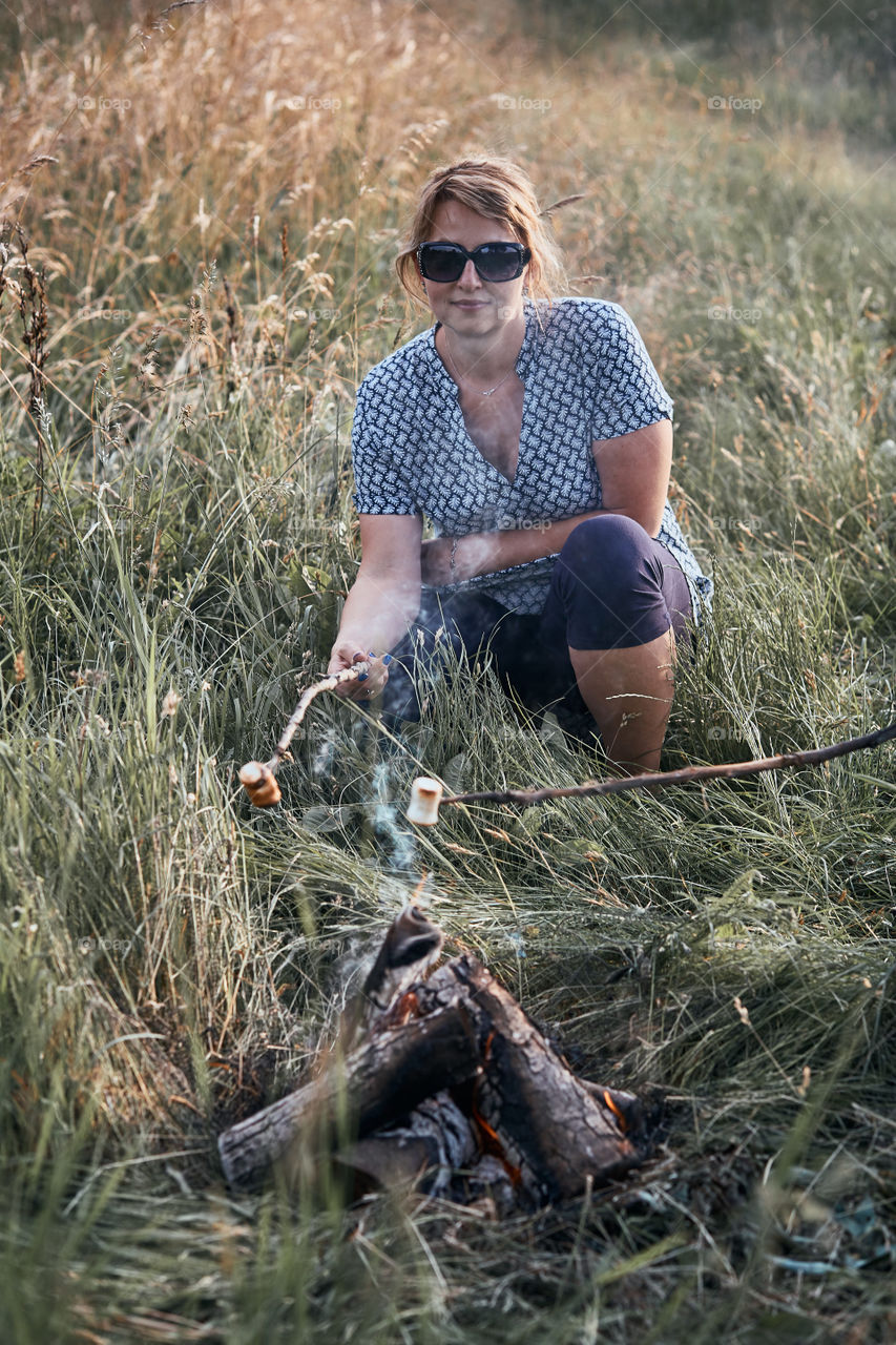 Women roasting a marshmallows over a campfire on meadow. Vacations close to nature. Candid people, real moments, authentic situations