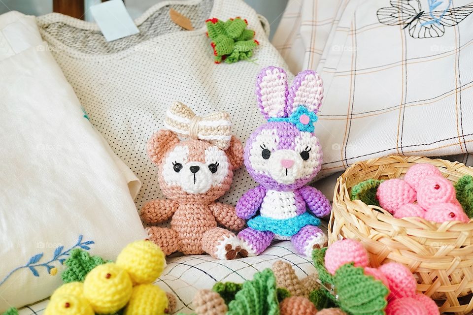 crochet dolls. a cute teddy bear and Easter bunny amigurumi doll, are sitting together with other crochet fruits at the weekend market.