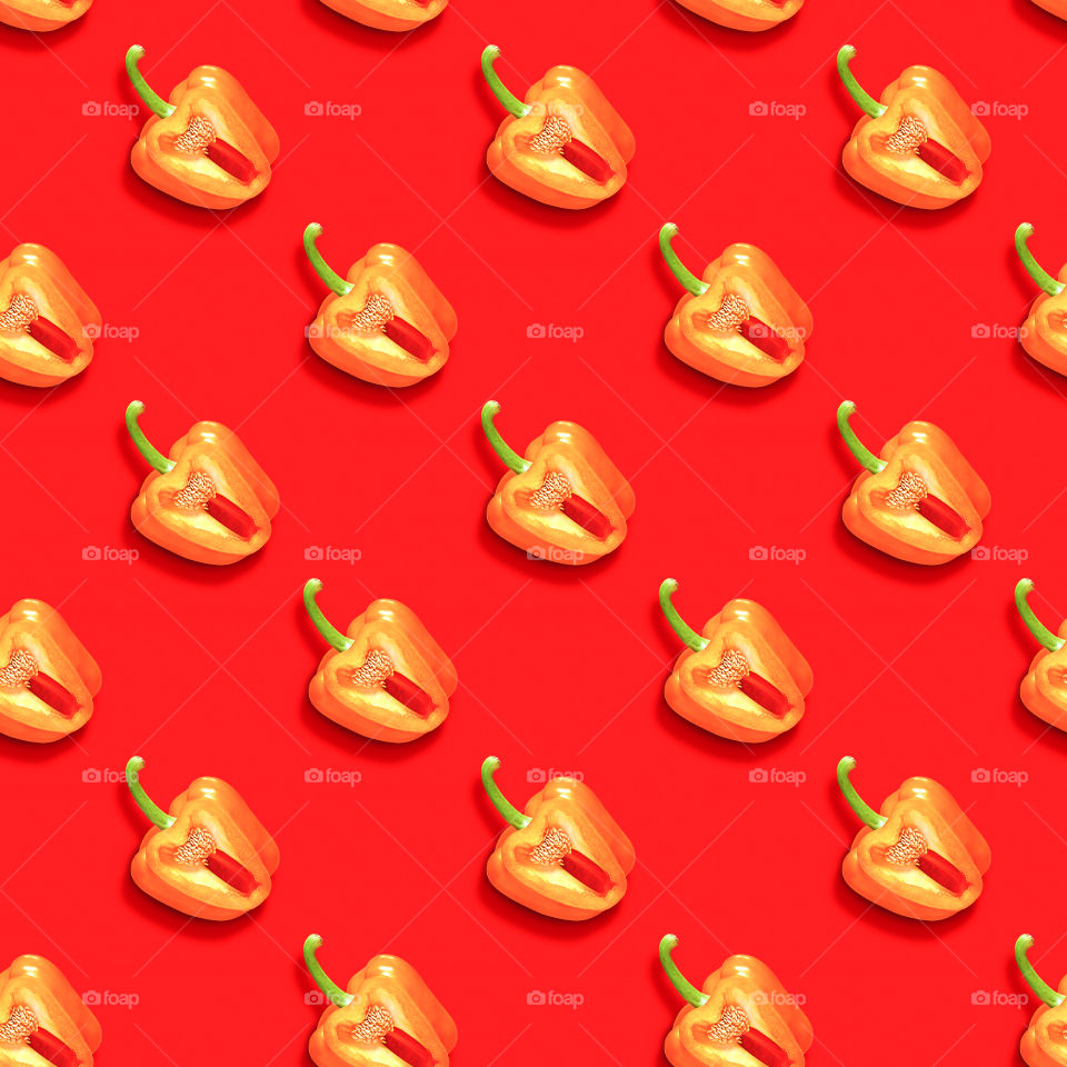 Repeating pattern of cut orange sweet bell peppers with green ponytails. The concept of healthy, ecological food. Beautiful contrasting ornament of fresh juicy pepper on a red background, top view, flat lay