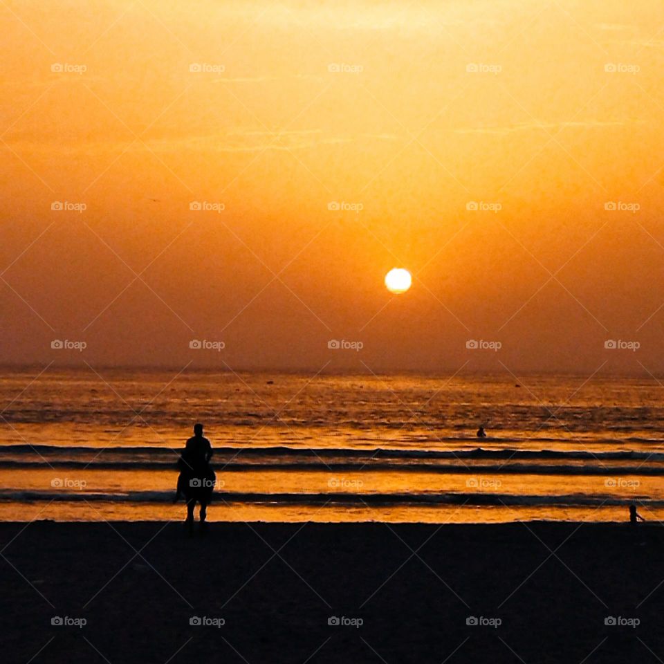 splendid sunset and beautiful young man riding on horseback towards the sea at essaouira city in Morocco.