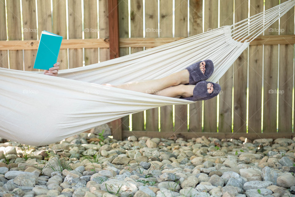 Woman wearing slippers and reading a book in a hammock