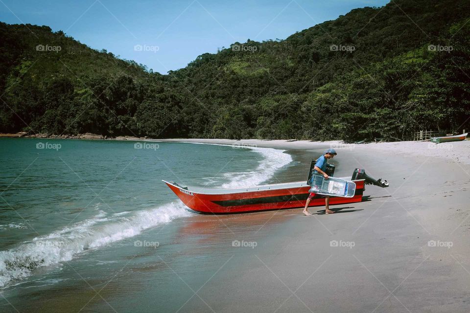 Sailor with his boat on the beach, getting Supplies, at Ubatuba, Brasil. He's bringing chairs to a resort, in a Beautiful Sunny day.