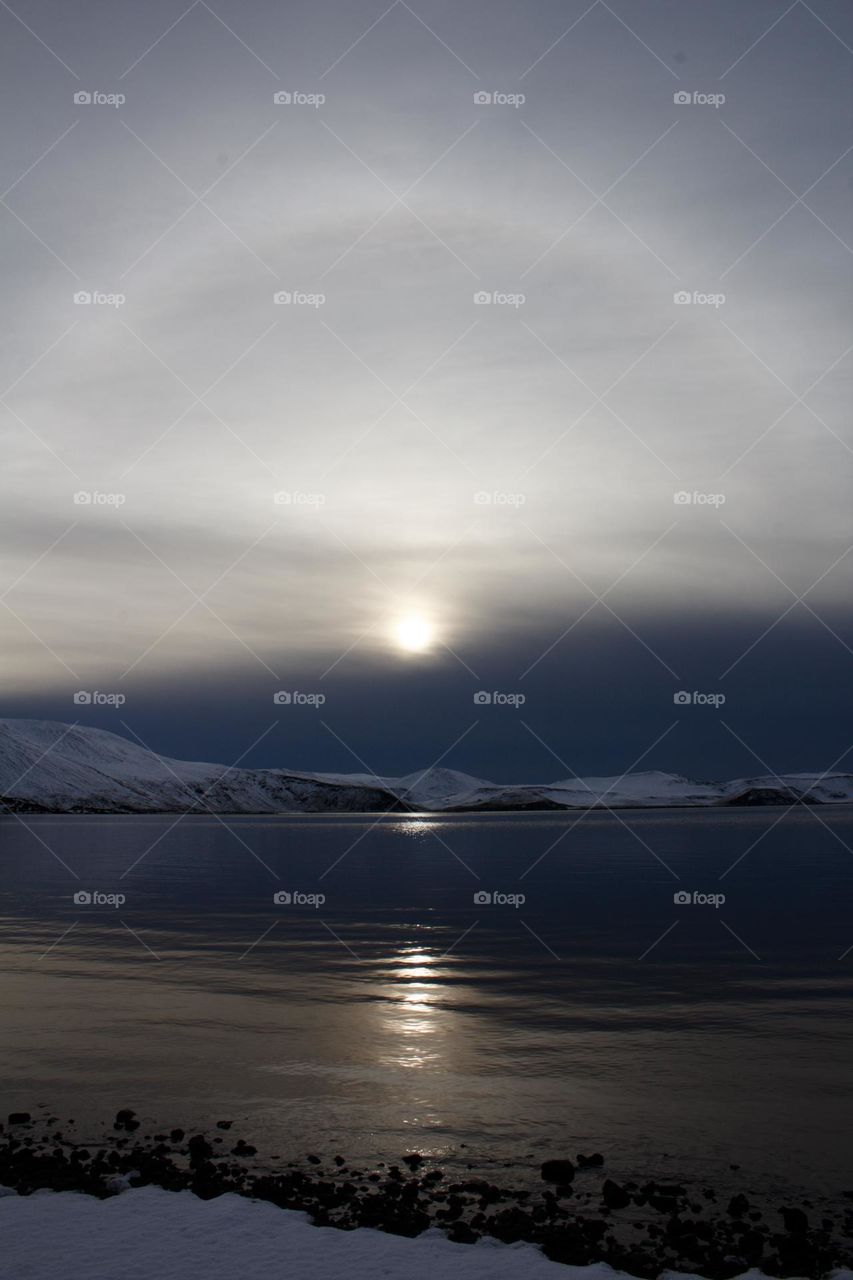 Zen picture of a calm lake in Iceland with sun aureole above.