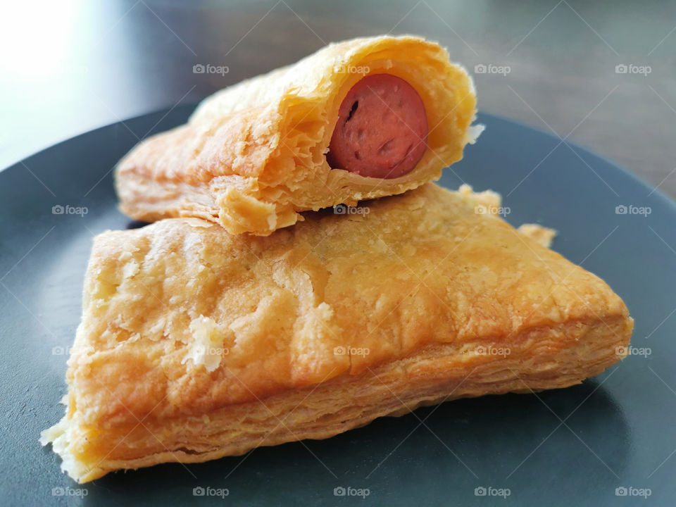 Sausage roll in a black blue plate on wood brown table.