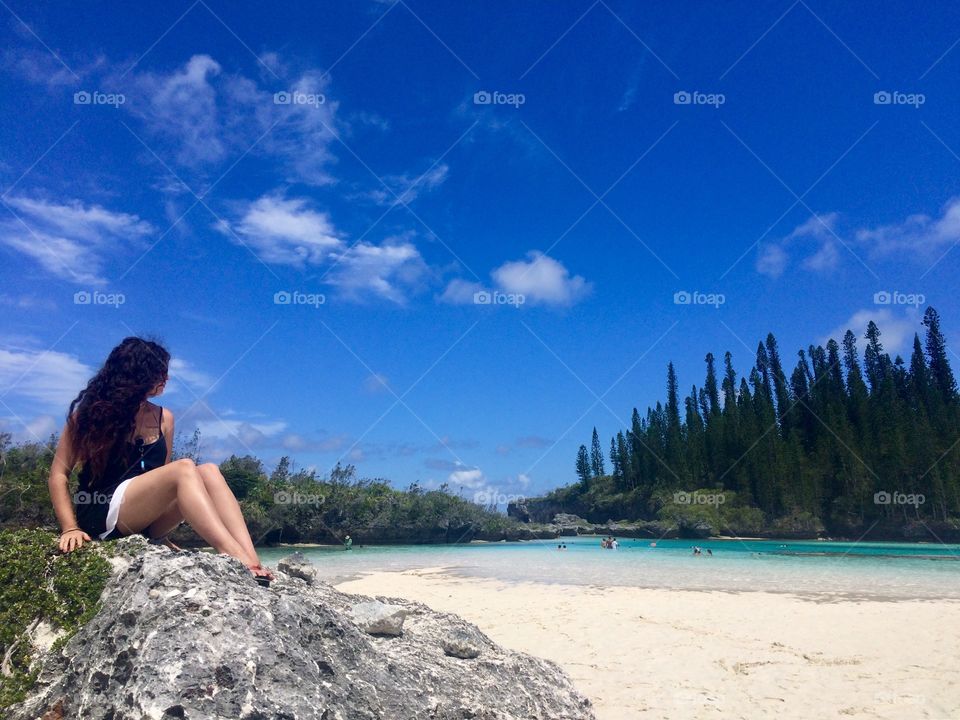 Young woman sitting on a rock of a paradise beach from the most beautiful lagoon of the Pacific