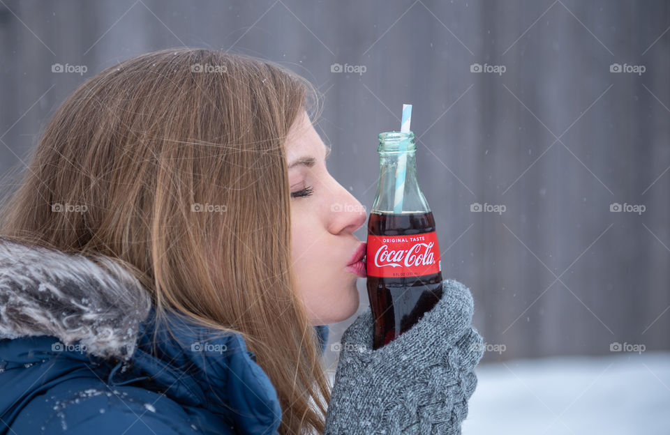 Close-up of a millennial woman kissing a bottle of Coca-cola outdoors in the snow