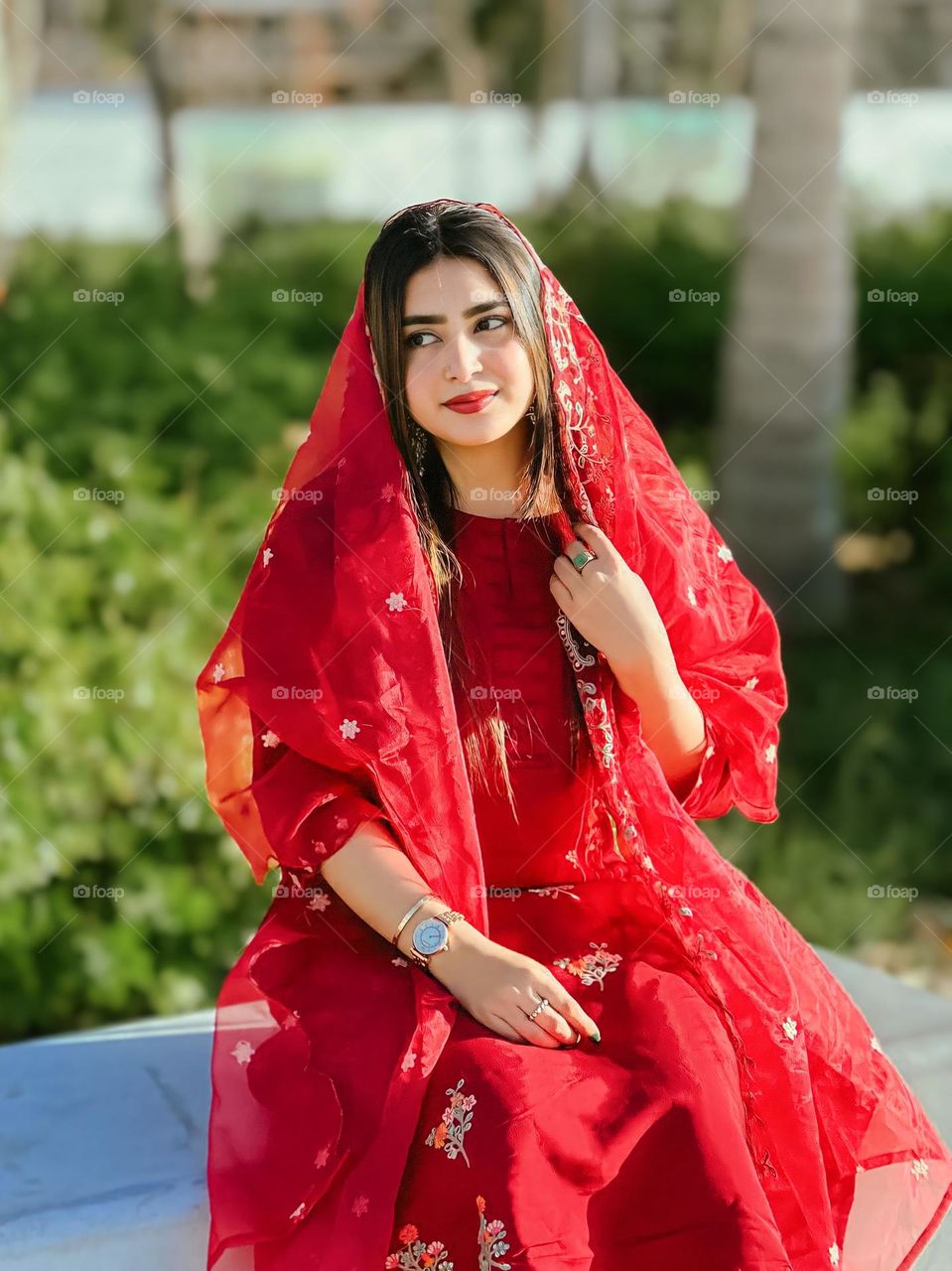 Close-up view of young woman from wearing traditional clothes with beautiful garden background. She looked graceful and elegant in a red dress and shawl of the same color