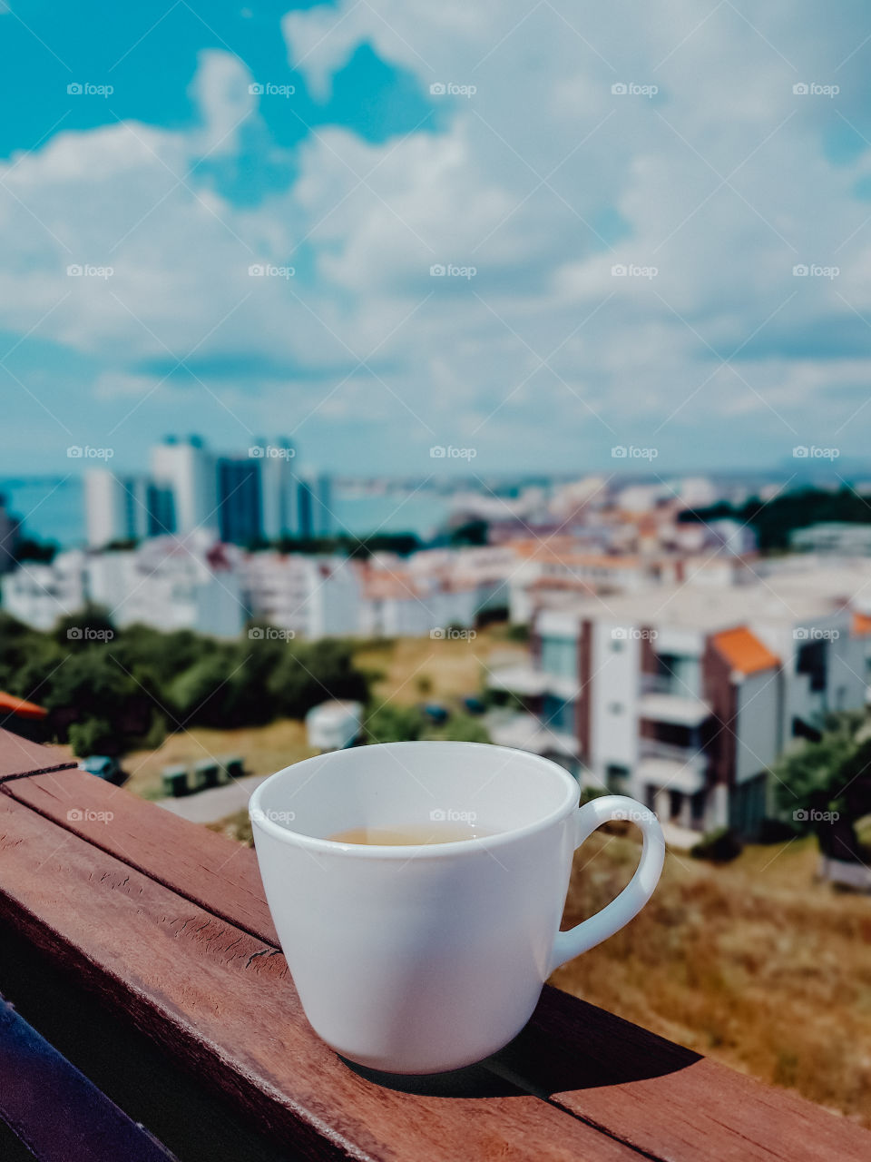 A cup with tea on balcony with cityscape view.