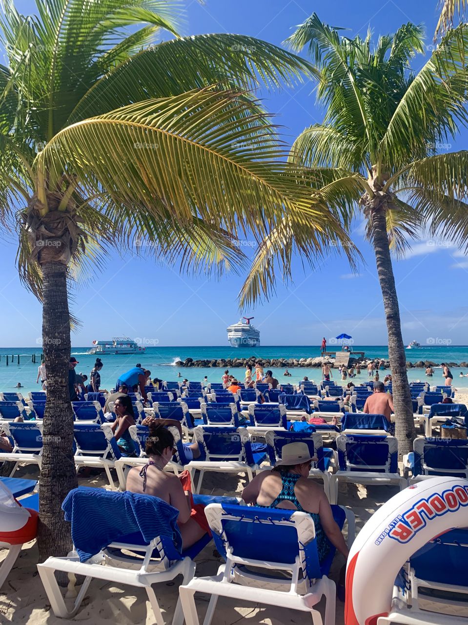 People in lawn chairs on the sandy beach with cruise ship in the background