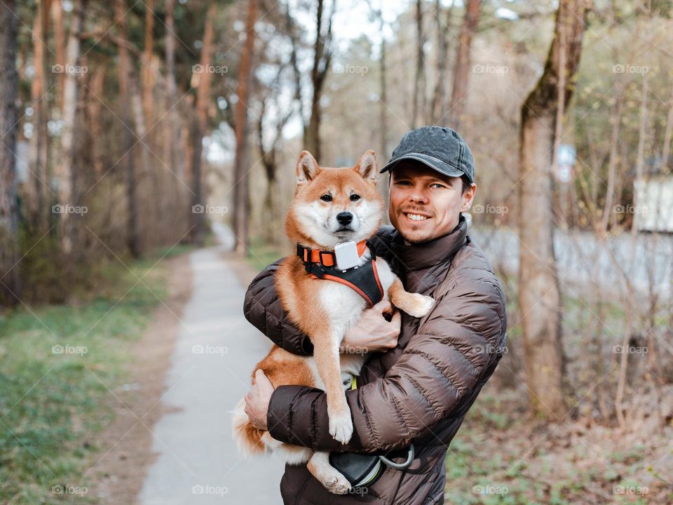Male hugs a cute shiba inu dog puppy candid portrait outdoor while walking