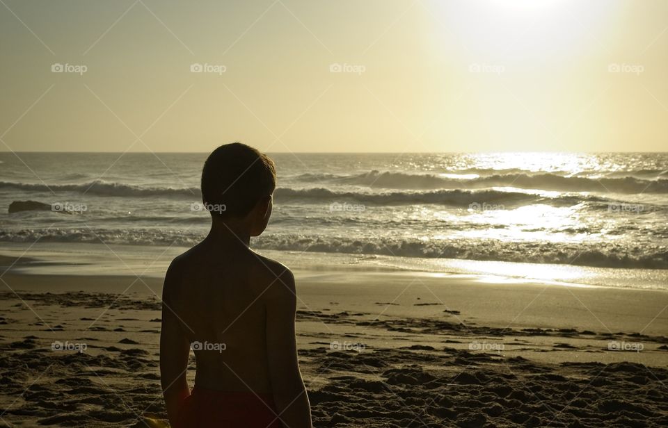 Boy looking at the sea at sunset 
