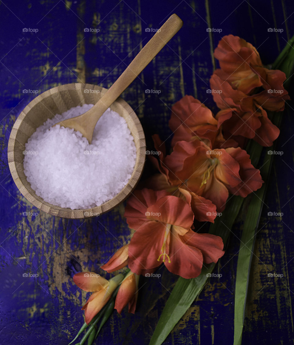 salt in a wood bowl with flowers in blue wood background