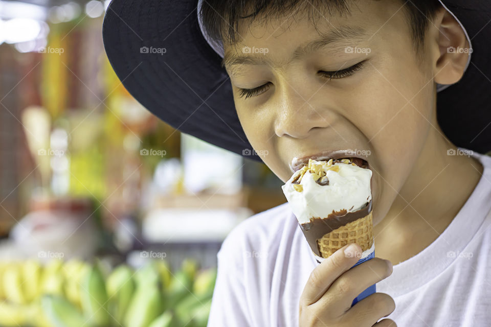 Asian Boys wearing a hat eating ice cream cone in hand.