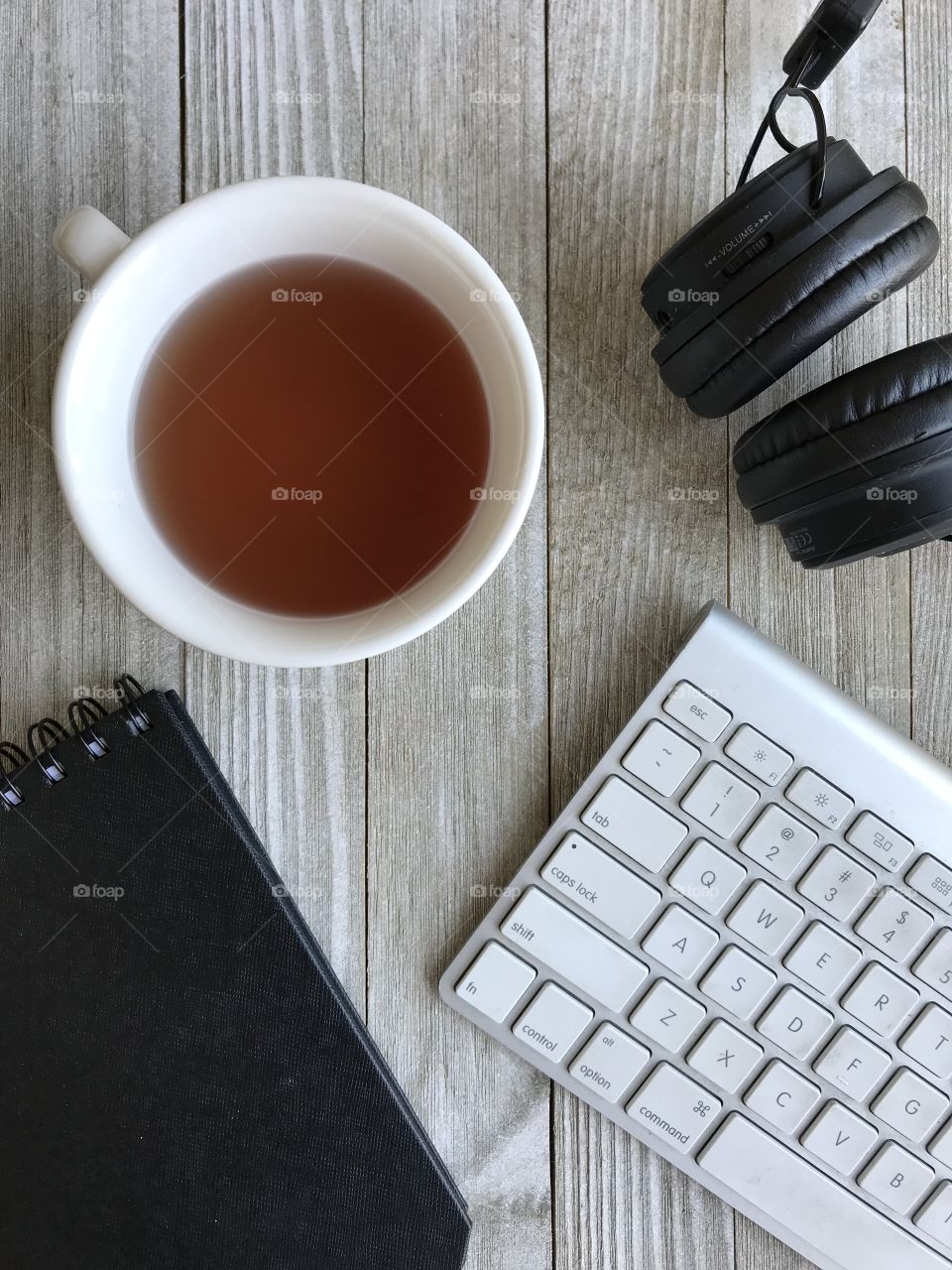 Looking down on a table which has a cup of tea along with a keyboard, notebook and headphones getting ready to start the day!!