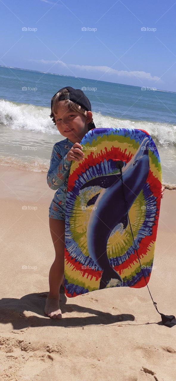 blond boy with colorful surfboard on the beach in Porto Seguro.