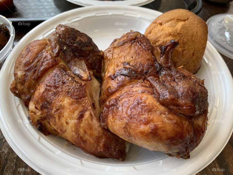 Half roasted chicken in a round white plastic plate with corn muffin. Mash potato.