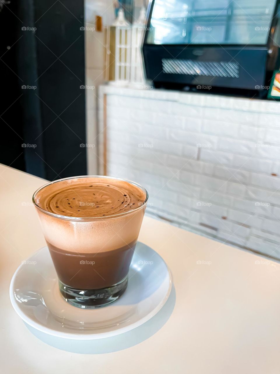 A cup of hot cappuccino in a clear cup on a white table top