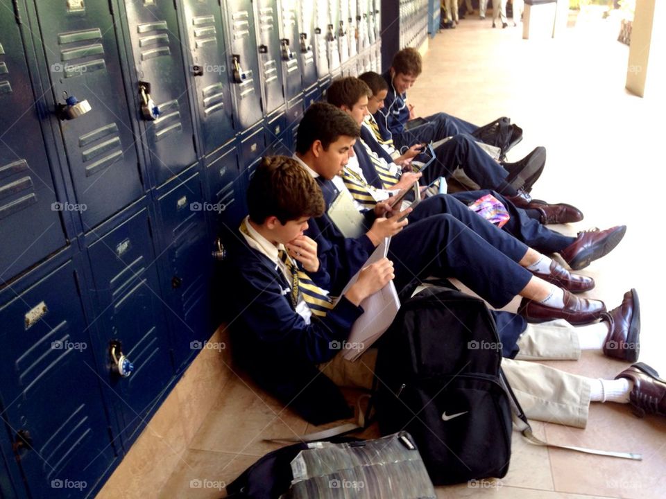 Students sitting on school corridor using iPads
