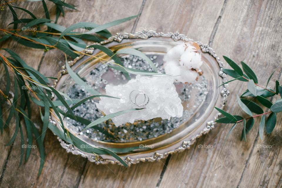 Silver plate with two wedding ring and white crystal on wood background.