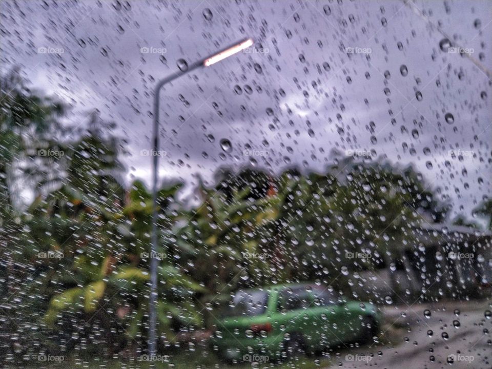 A car and lamp post is visible through raindrops on another car window on a rainy day