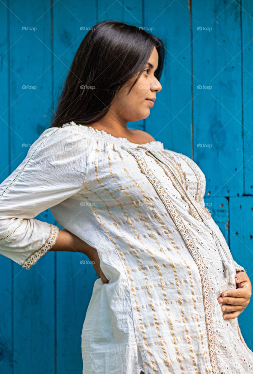 Mulher grávida de roupa branca e fundo azul.