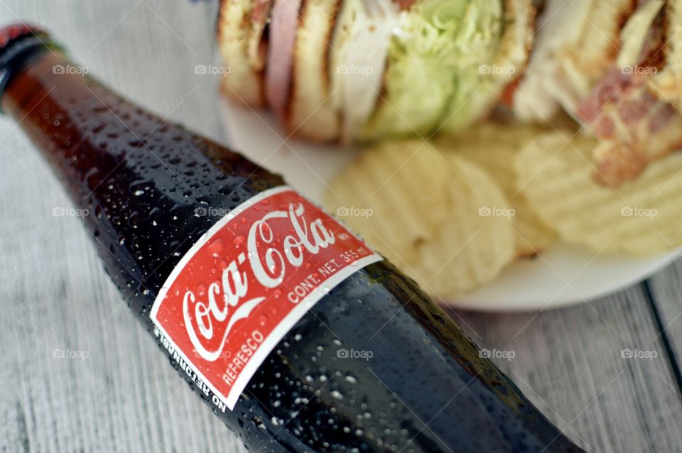 A can and a Bottle of Coca Cola with a club sandwich on a white rustic background 