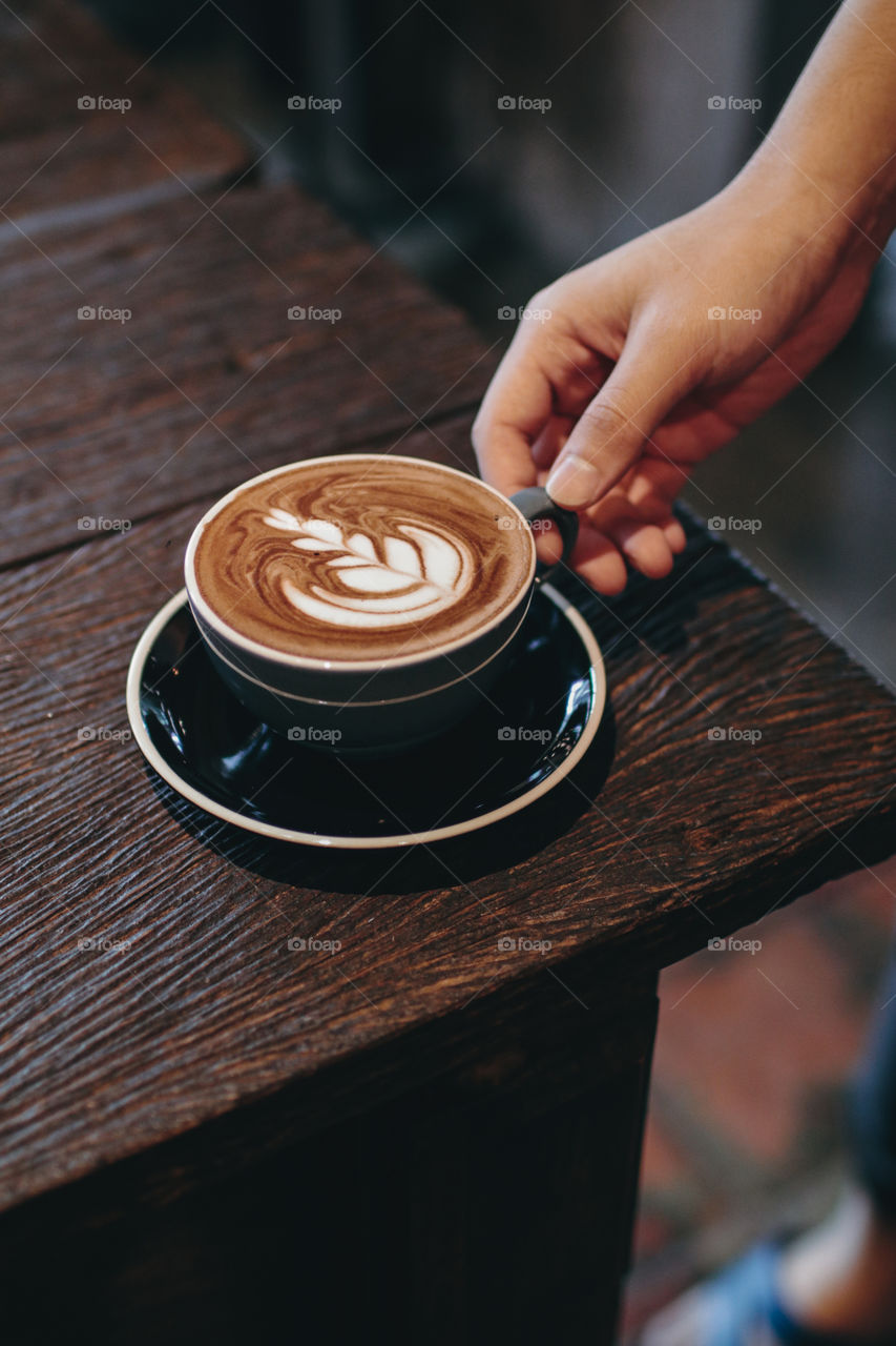 Hot coffee latte on wooden table holding with one hand