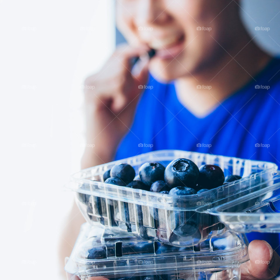 Close up fresh organic blueberries in plastic boxes with healthy young man holding and eating blueberry blur background 