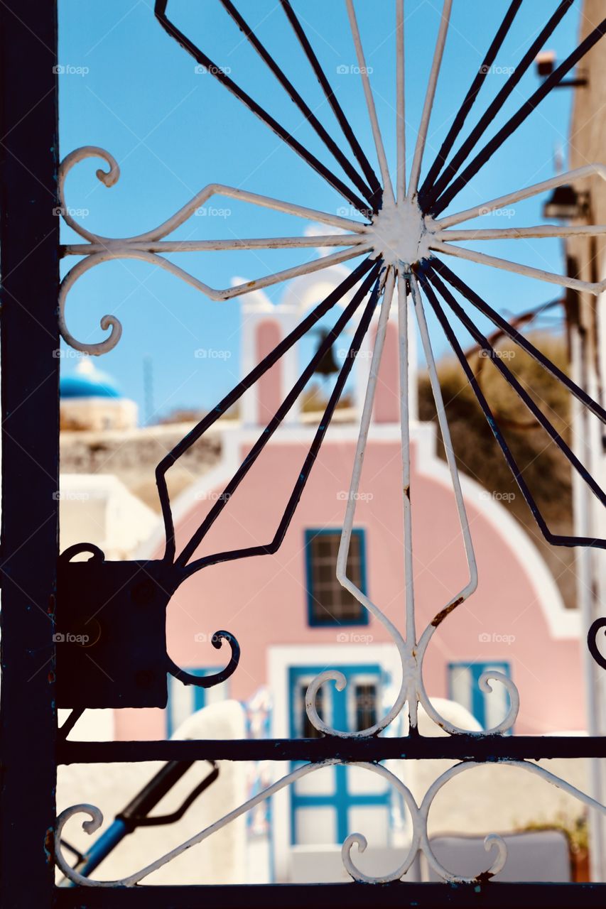 Looking out the window through the ornamental iron safety across the street to the pink colored church tower 