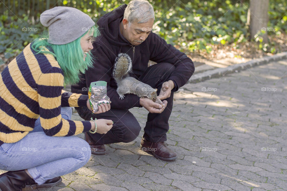 Alternative girl with green hair and old man feeding a squirrel