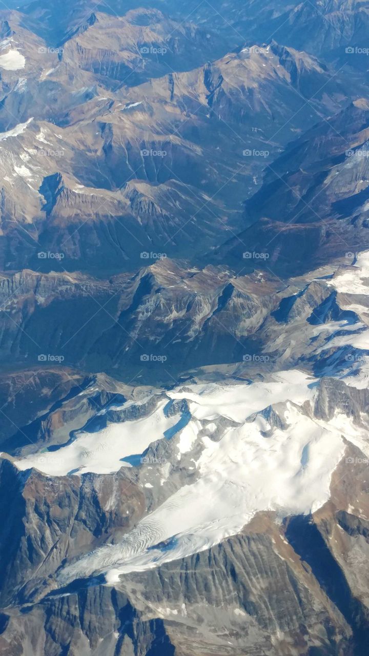 Flying over magnificent mountain peaks of Canada with flowing glaciers and aquamarine meltwater lakes on their summits.