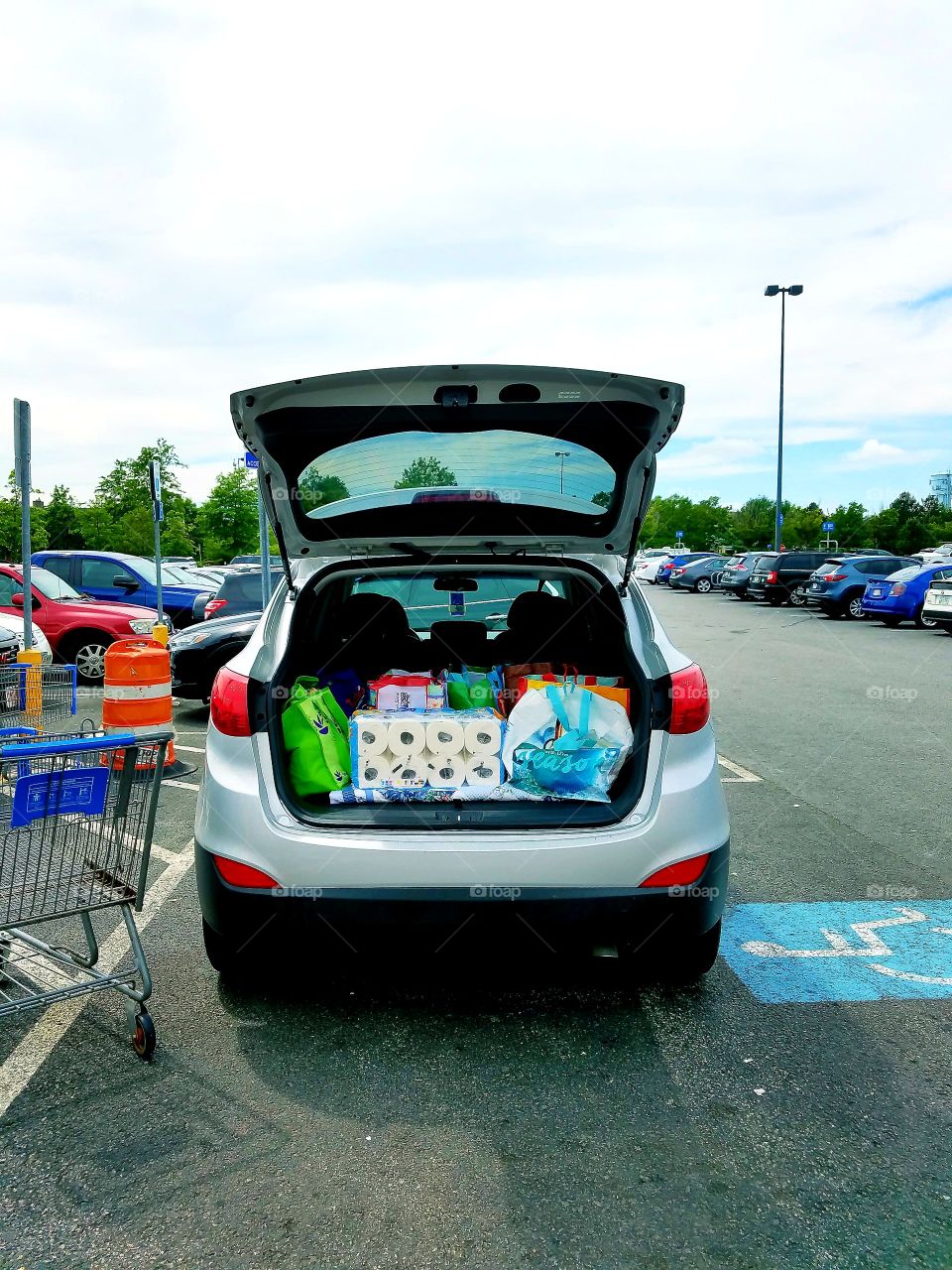 Shopping Bags in car, busy parking lot. Handicapped. Trunk open.