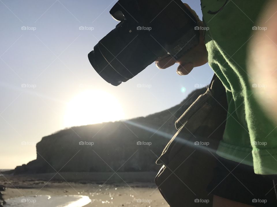Camera in hand, a photographer walks along the beach in search of the best coastal shot. 
